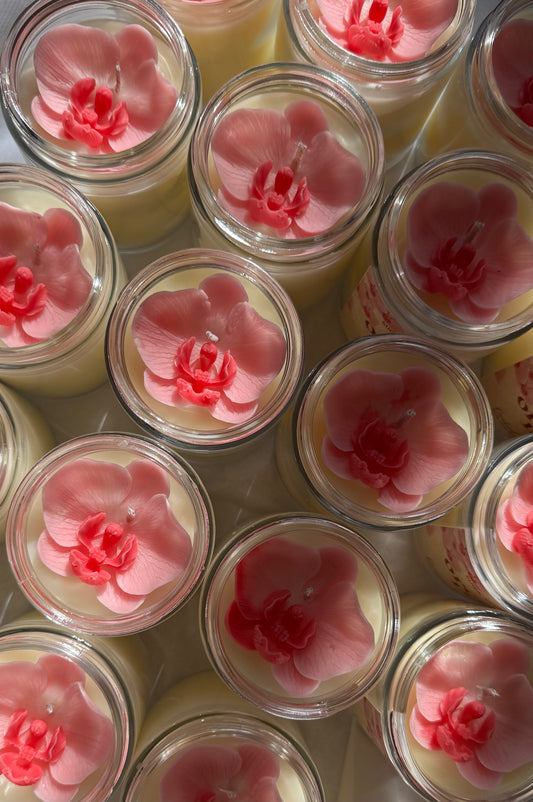 Jars of candles with pink floral orchid designs on a white background
