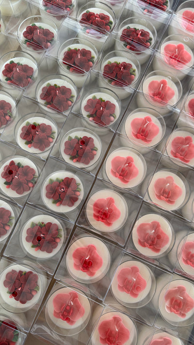 Plastic packaging with small pink orchid and plumeria flowers inside, arranged in a grid pattern.